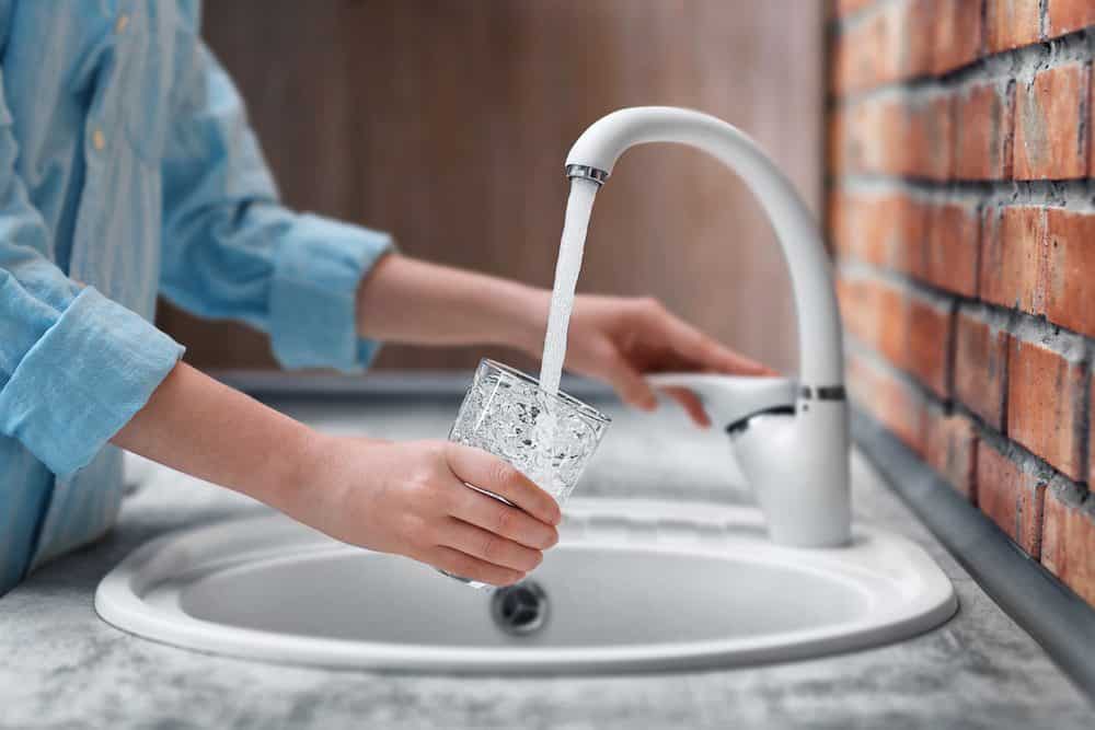 Woman fills glass with clean water from sink connected to whole house water filters